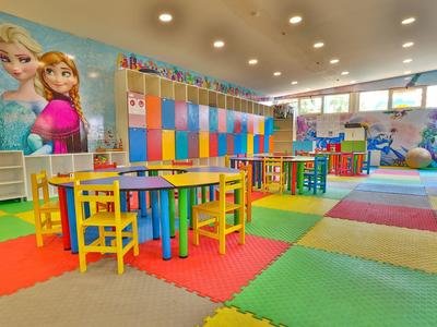 Barevná dětská herna se stoly, židlemi a velkou nástěnnou dekorací postaviček z Disney.