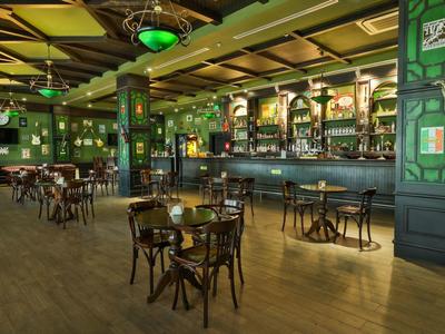 Příjemný bar s dřevěnými stoly, židlemi a zeleně dekorovaným interiérem.