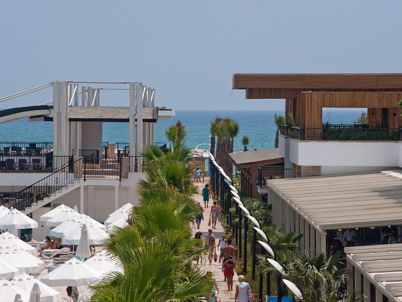 Pohled na hotelovou cestu s bílými slunečníky, palmy a moře v pozadí.