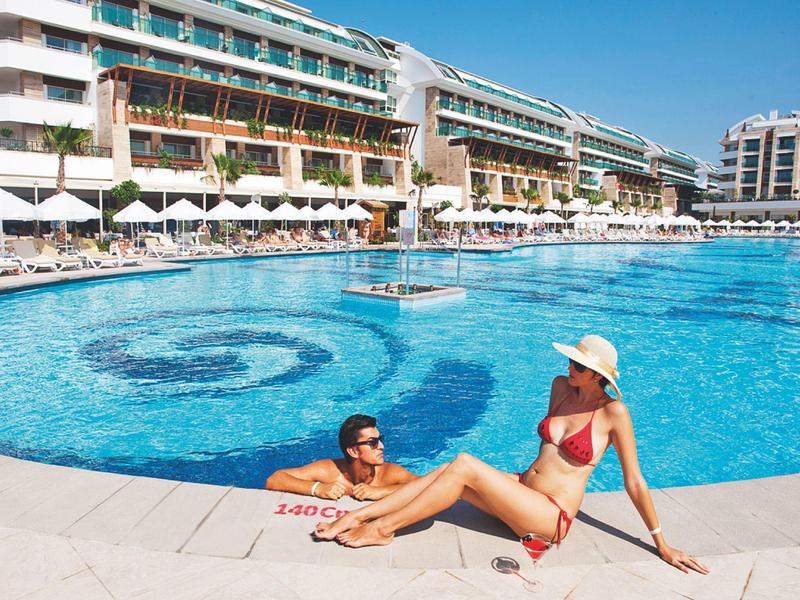 Žena a dítě odpočívají na okraji velkého hotelového bazénu za slunečného dne.