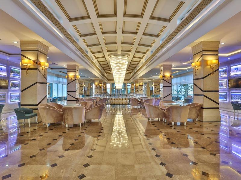 Prostorná luxusní hotelová lobby s lesklou mramorovou podlahou, čalouněnými křesly a osvětlenými stěnami.