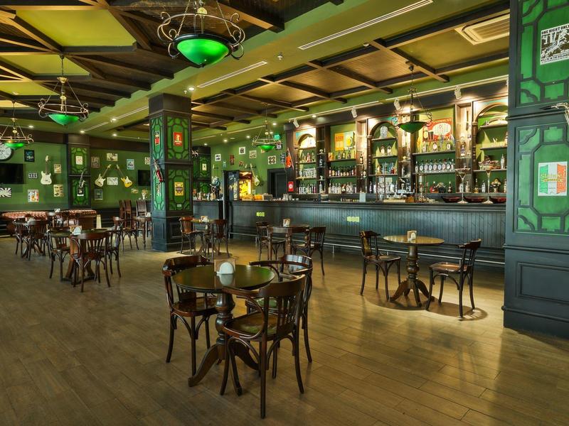 Příjemný bar s dřevěnými stoly, židlemi a zeleně dekorovaným interiérem.
