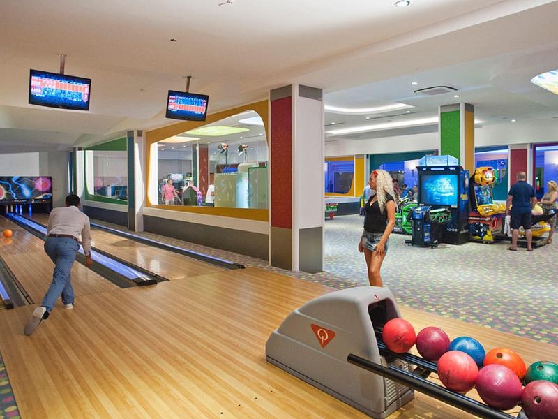 Několik lidí hraje bowling v dobře osvětlené dráze s barevnými bowlingovými koulemi.