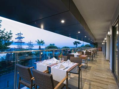 Vista su una terrazza con tavoli apparecchiati che si affacciano su palme e mare al crepuscolo.