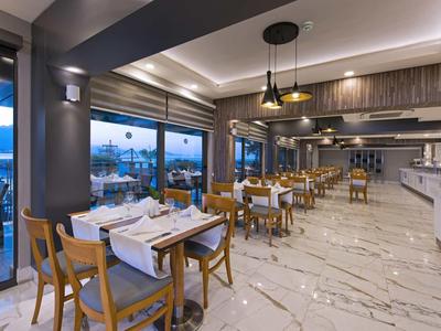 Ristorante moderno con sedie in legno, tavoli apparecchiati e grande finestra panoramica con vista mare.