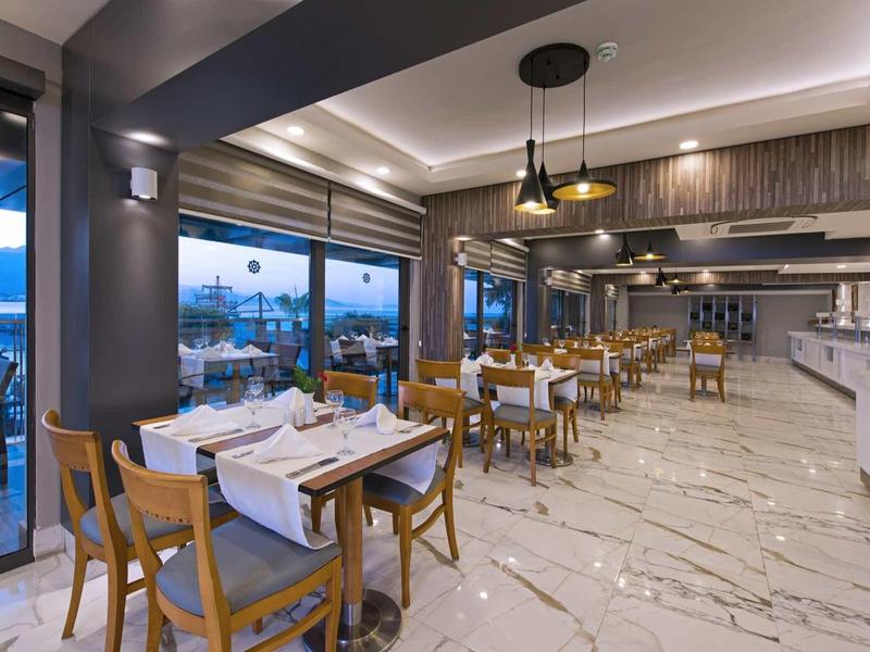 Ristorante moderno con sedie in legno, tavoli apparecchiati e grande finestra panoramica con vista mare.