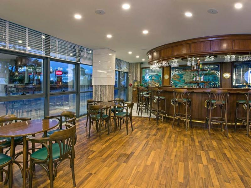 Bar vuota con pavimento in legno e tavoli in una stanza d'hotel con grande finestra.