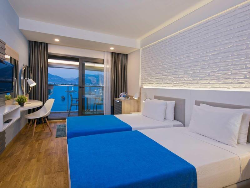 Camera d'hotel moderna con due letti singoli, grande finestra e TV a parete.