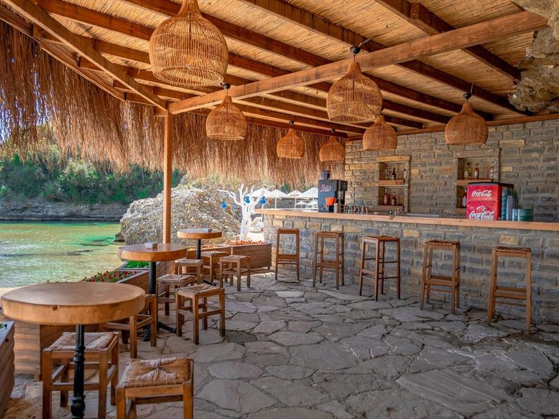 Rustikales Outdoor-Café mit Holz- und Steinelementen, Stroh-Dach und Blick auf eine grüne Landschaft.