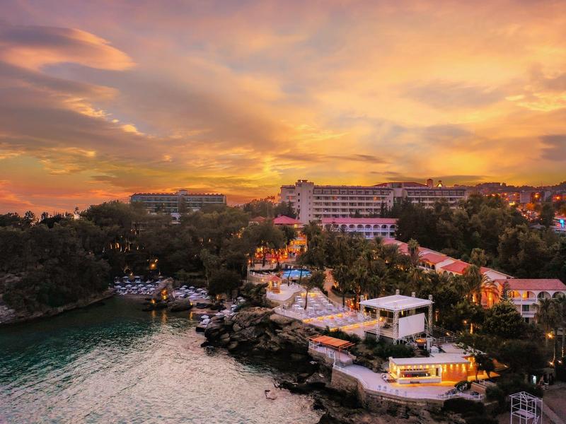 Küste mit Felsen, Häusern und leuchtendem Sonnenuntergangshimmel in Orange- und Violetttönen.