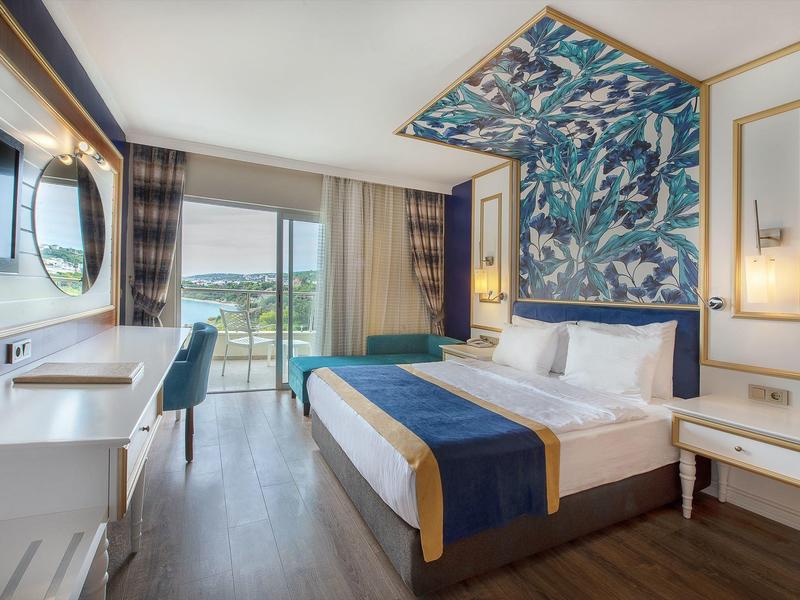 Modernes Hotelzimmer mit großem Bett, blauer Deko, Holzboden und Blick auf See und Berge.