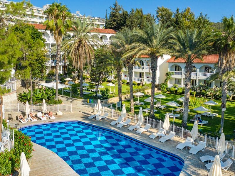 Schöner Außenpool mit blauem kariertem Boden, umgeben von weißen Liegestühlen und Palmen im Hotelgarten.