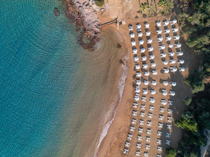 Luftaufnahme eines Strandes mit klar blauem Wasser, Sand und symmetrisch angeordneten weißen Sonnenschirmen.