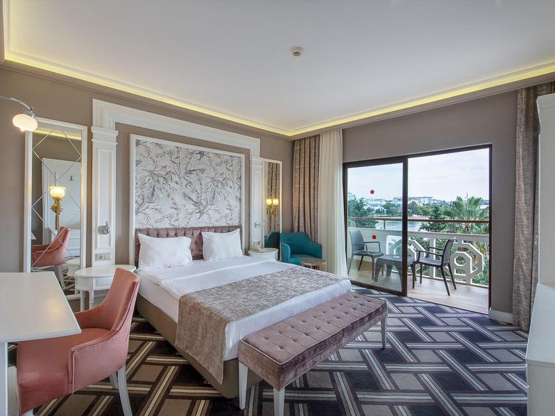 Modernes Hotelzimmer mit großem Bett, Schreibtisch, Sofa und Balkon mit Blick ins Grüne.