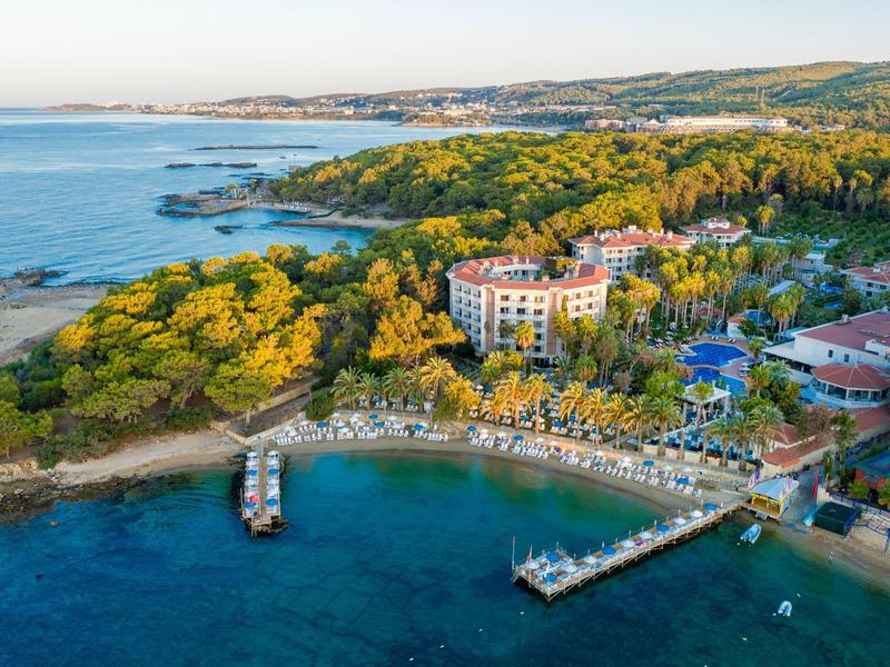 Luftaufnahme eines Küstenresorts mit türkisblauem Meer, Sandstrand, grünen Bäumen und Gebäuden.
