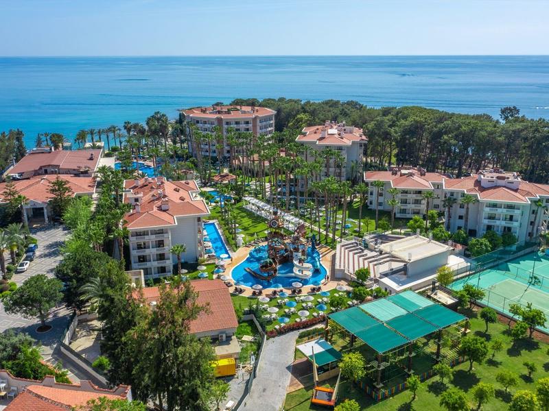 Hotelanlage mit mehreren Gebäuden, Pools, Tennisplatz, Palmen und Blick auf das blaue Meer.