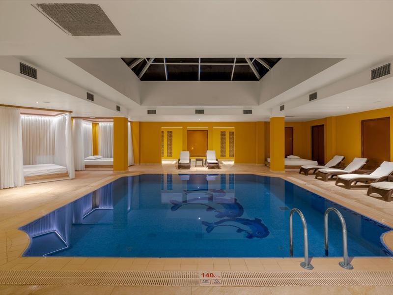 Innenpool mit blauen Wasser, weißen Liegen und gelben Wänden in einem modernen Raum.