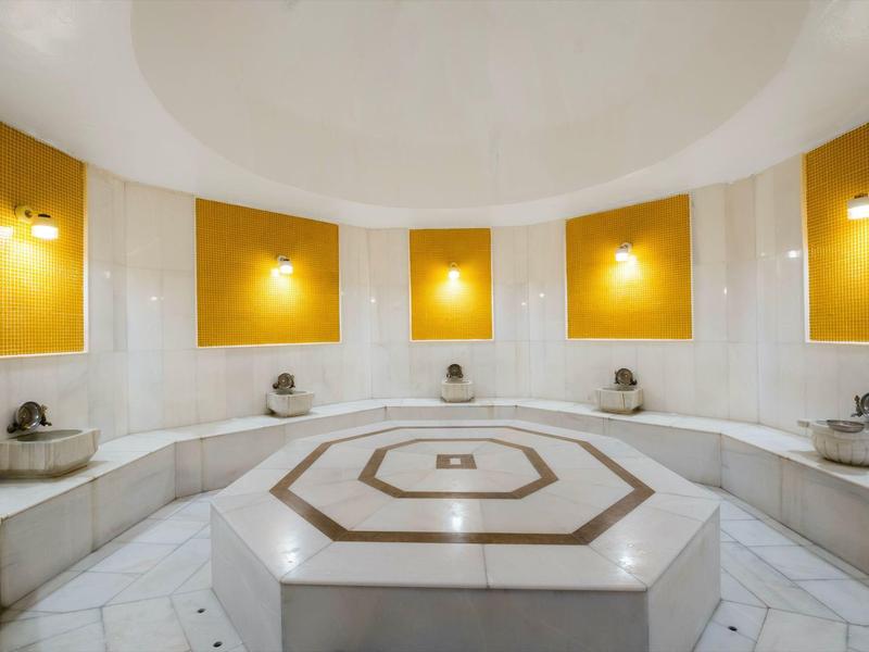 Heller, runder türkischer Hamam mit Marmor, gelben Wänden und zentralem beheiztem Steinblock.