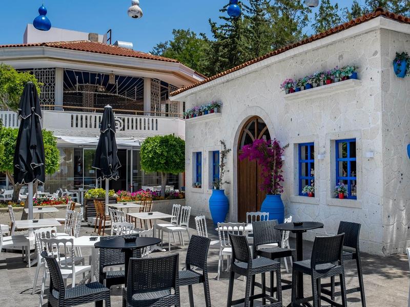 Außenbereich eines Cafés mit weißen und schwarzen Tischen und Stühlen, blauen Dekorationen, klarer Himmel.