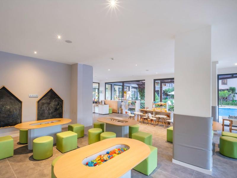 Heller Raum mit moderner Kinder-Spielecke, bunten Sitzhockern und Holzmöbeln, Fenster mit Außenblick.