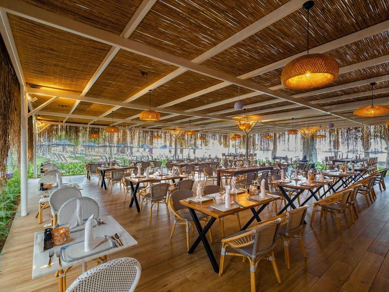 Großer, offener Restaurantbereich mit Holztischen, Stühlen, Bambusdecke und warmen Lampen.