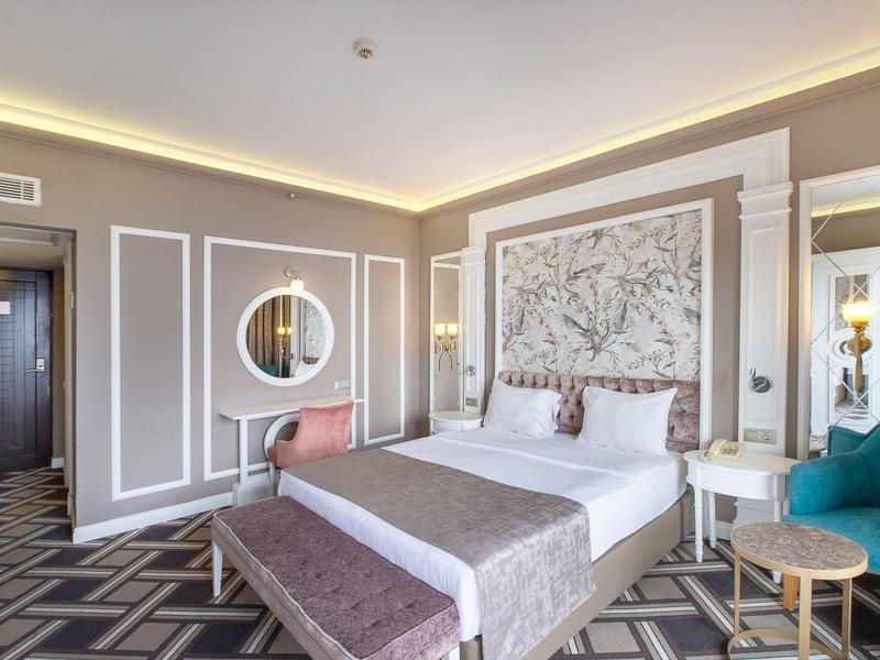 Modernes Schlafzimmer mit großem Bett, gemustertem Teppich, rundem Spiegel und grüner Sitzgruppe.