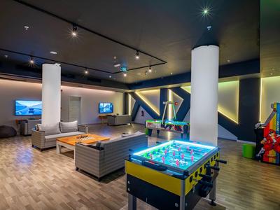 Moderner Freizeitraum mit Kicker, Sitzgruppen, Fernsehern und bunten LED-Lichtern an den Wänden.