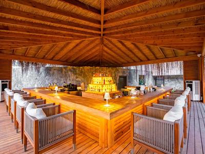 Offener Pavillon mit hölzernem Dach und quadratischem Essbereich, umgeben von Stühlen mit Kissen.