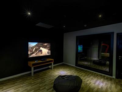 Dunkler Raum mit Holzfußboden, Fernseher auf Tisch, schwarzer Sitzsack und Spiegelfläche an der Wand.