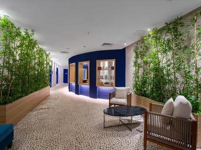 Moderner Flur mit Steinboden, blauen Wänden, grünen Pflanzen und Holzmöbeln mit Kissen.