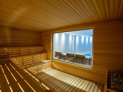 Sauna mit hellen Holzbohlen, breiten Sitzbänken und Fenster zur kühlenden Außenlounge.