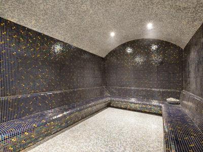Moderner Sauna-Ruheraum mit gebogenem Deckenbogen, dunklen Mosaikfliesen und hellem Steinboden.