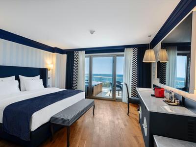 Camera d'hotel moderna con letto matrimoniale, balcone e vista mare.