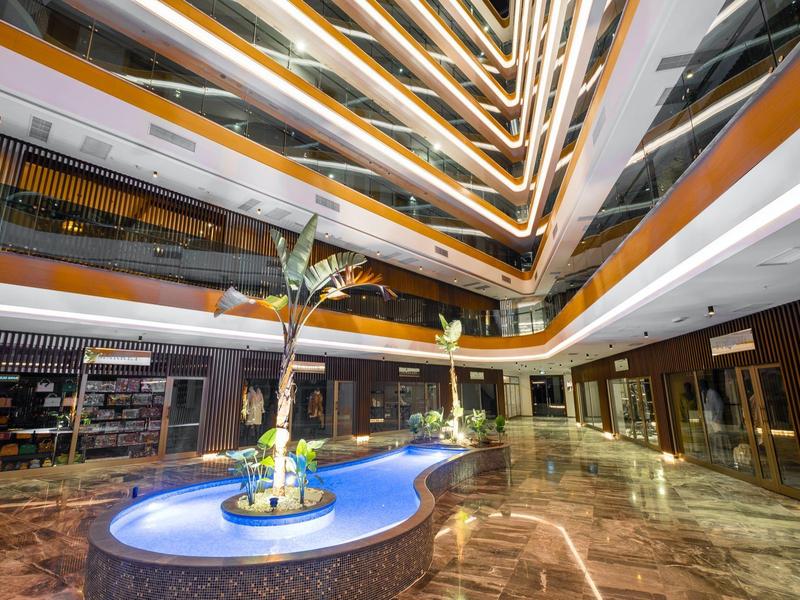 Modernes Atrium mit mehrstöckigem Gebäude, beleuchteter Brunnen, Palme und glänzendem Boden.