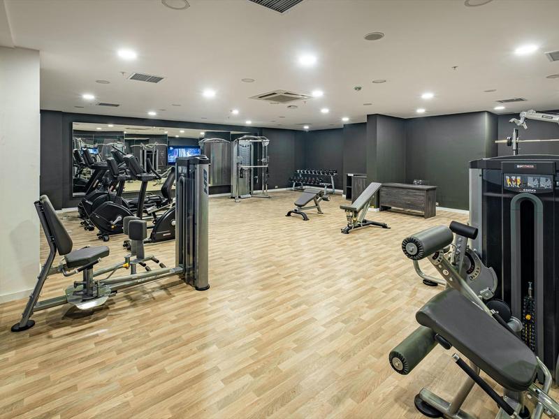 Modernes Fitnessstudio mit Holzboden, grauen Wänden und verschiedenen Trainingsgeräten.