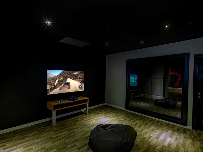 Dunkler Raum mit Holzfußboden, Fernseher auf Tisch, schwarzer Sitzsack und Spiegelfläche an der Wand.