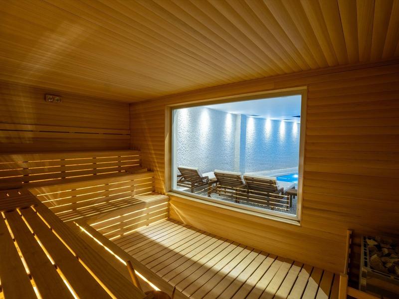 Sauna mit hellen Holzbohlen, breiten Sitzbänken und Fenster zur kühlenden Außenlounge.