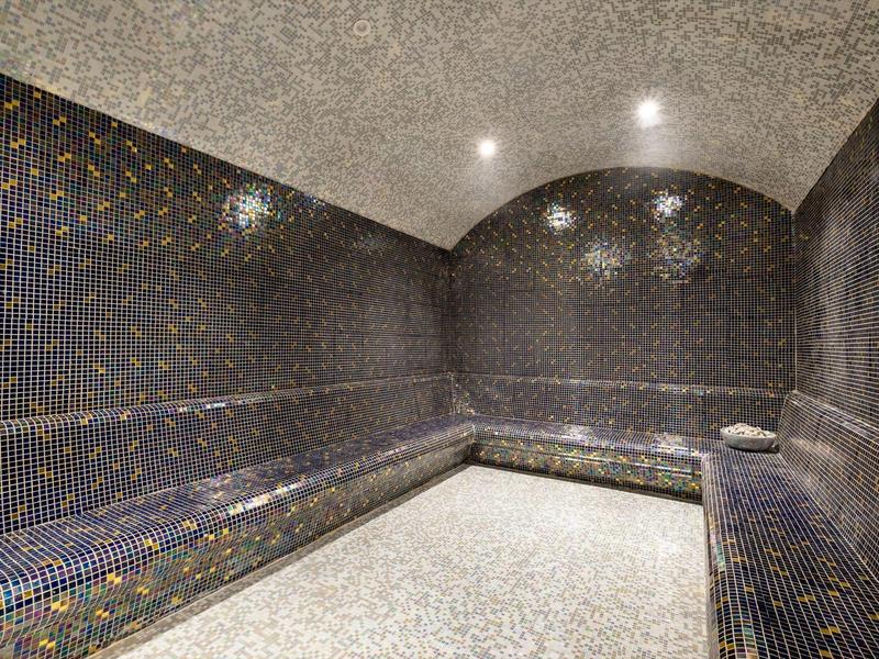 Moderner Sauna-Ruheraum mit gebogenem Deckenbogen, dunklen Mosaikfliesen und hellem Steinboden.