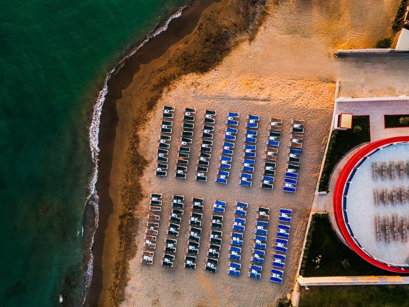 Vue aérienne d'une plage avec des transats bleus et du sable près de la mer turquoise.