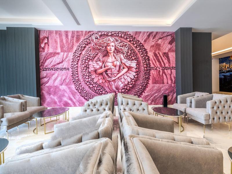 Salon d'hôtel moderne avec fauteuils gris et grande œuvre murale rose.