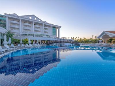 Duży basen hotelowy z leżakami i budynkami w tle pod bezchmurnym niebem.