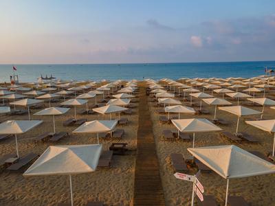 Reihe von weißen Sonnenschirmen auf einem Sandstrand mit Blick auf das ruhige Meer bei Sonnenuntergang.