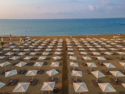 Symmetrisch angeordnete Sonnenschirme auf einem Sandstrand mit Blick auf das ruhige Meer.