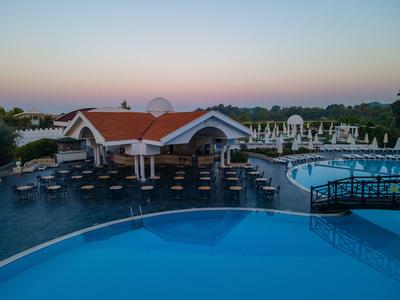 Großer Außenpool mit Liegestühlen und einem Gebäude im Hintergrund bei Sonnenuntergang.