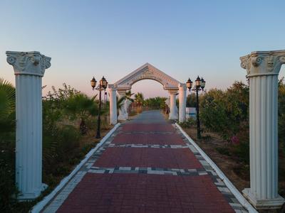 Mittelgang mit roten Kacheln und weißem Tor, flankiert von antiken Säulen und Laternen im Freien.