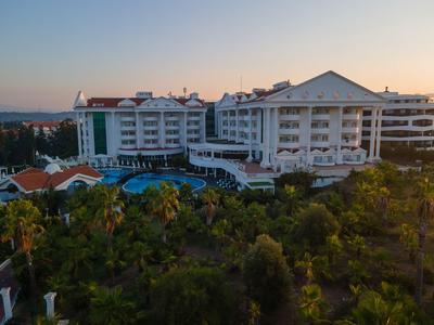 Großes Hotelgebäude mit Pool und viel Grün bei Sonnenuntergang.