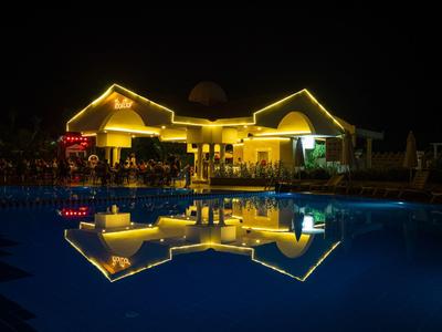 Beleuchtetes Hotelgebäude mit Pool, dessen Spiegelung das Gebäude bei Nacht zeigt.