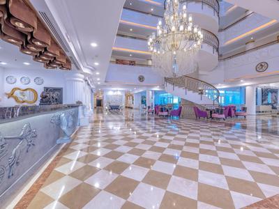 Helles Hotelfoyer mit Marmorboden, Empfangstresen, Wendeltreppe und Kronleuchtern.
