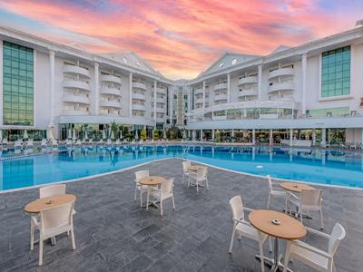 Modernes Hotel mit großem Außenpool und Sitzbereichen unter einem rosa Sonnenuntergang.