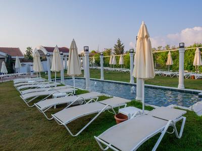 Weiße Liegestühle und geschlossene Sonnenschirme am Pool in einer Hotelanlage.